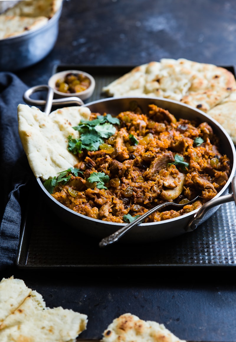 Handi of slow-cooked curry with naan, shot in warm low light